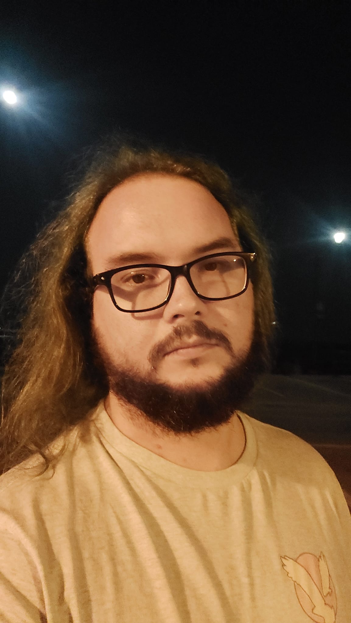 A man with hair that looks brown and shirt that looks yellow stands under a monochromatic street light